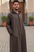 Man wearing an olive-brown hooded Moroccan thobe by a mosque doorway